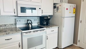 A kitchen with white cabinets, a microwave, a stove, a coffee maker, and a refrigerator. - Elegant Egret 4 Bedroom Home by RedAwning (Supply)