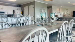 A modern kitchen with white cabinets, a dining area with a wooden table and chairs, and a living room with a sofa and decorative wall art. - Elegant Egret 4 Bedroom Home by RedAwning (Supply)