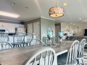 A modern kitchen with white cabinets, a dining area with a wooden table and chairs, and a living room with a sofa and decorative wall art. - Elegant Egret 4 Bedroom Home by RedAwning (Supply)