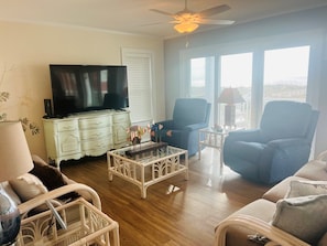 A living room with a flat-screen TV on a white dresser, two blue armchairs, a white coffee table, and a ceiling fan. - Elegant Egret 4 Bedroom Home by RedAwning (Supply)