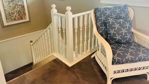 A staircase with white balusters, a cushioned chair with a starfish pattern, and a framed artwork of a bird and eggs. - Elegant Egret 4 Bedroom Home by RedAwning (Supply)