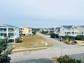 A residential street with multi-story houses, a grassy area, and a clear sky. - Elegant Egret 4 Bedroom Home by RedAwning (Supply)