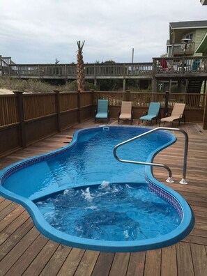 A swimming pool with a wooden deck, surrounded by a wooden fence and a palm tree.