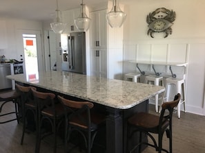 A kitchen with a large island, bar stools, pendant lights, and a clock on the wall. - Almost Heaven 4 Bedroom Home by RedAwning (Supply)