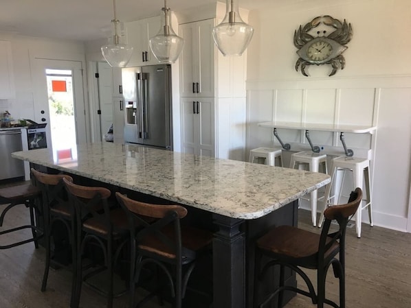 A kitchen with a large island, bar stools, pendant lights, and a clock on the wall.