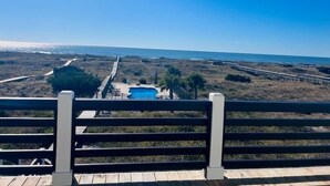 A beach view from a wooden deck with a pool and a boardwalk leading to the ocean.