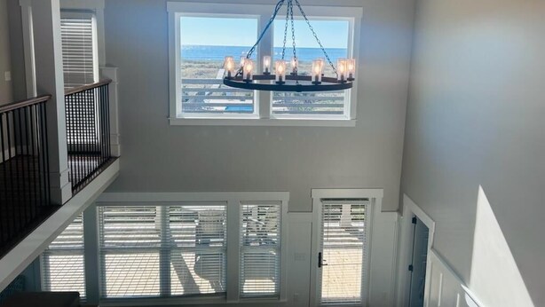 A high-ceiling room with a central chandelier, large windows, and a view of the outside.