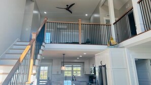 A spacious, multi-level interior with a staircase, a ceiling fan, and a kitchen area.