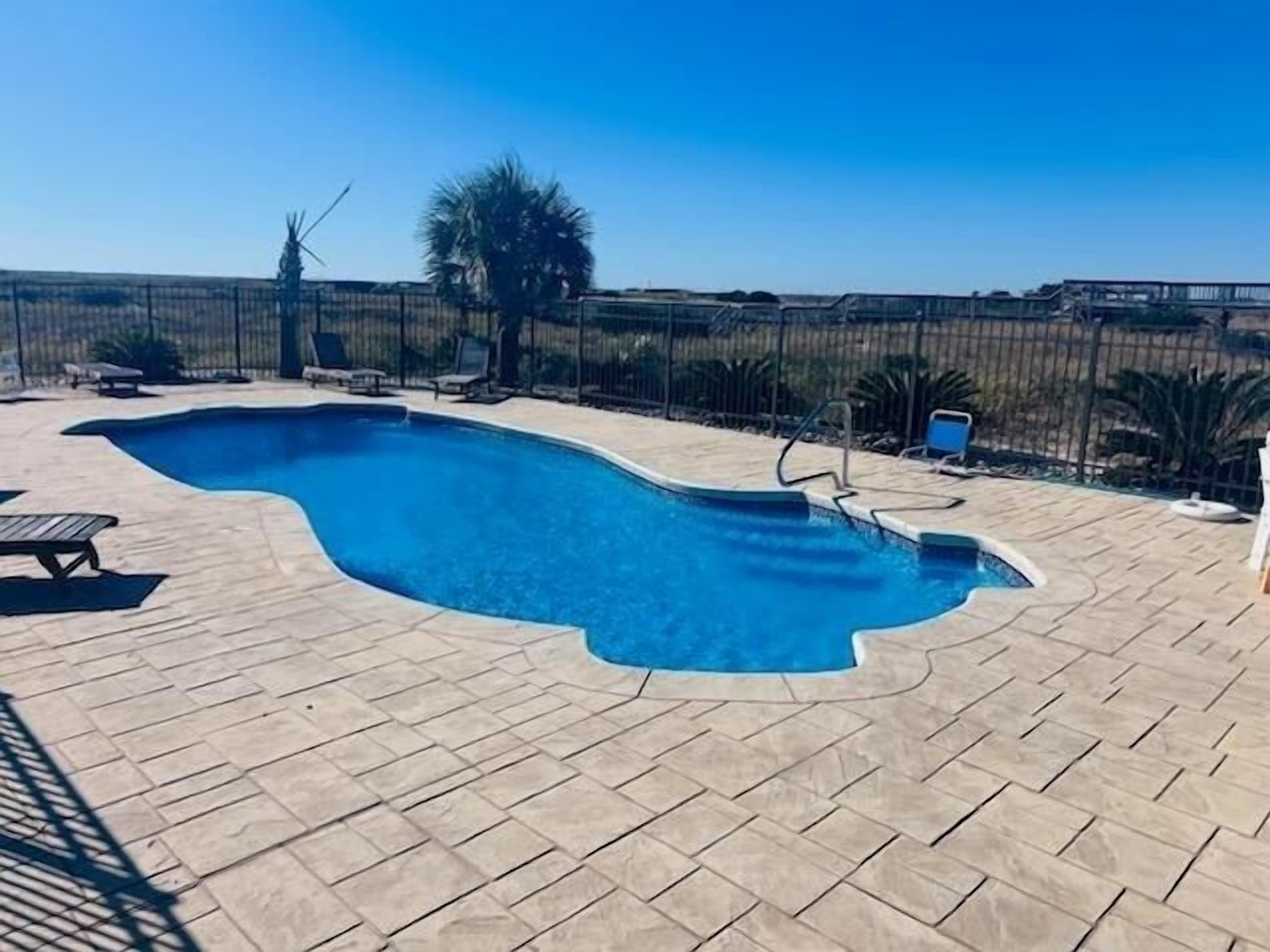 A swimming pool with a wavy edge, surrounded by a tiled deck and a metal fence.