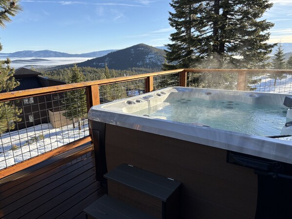 Ein Whirlpool auf einer Holzterrasse mit Blick auf schneebedeckte Berge und Kiefern.