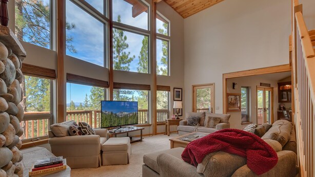 A spacious living room with large windows, a fireplace, and a television. - Northstar Conifer Luxury 5 Bedroom Home by RedAwning (Truckee)