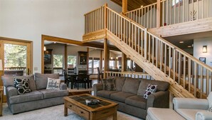 A spacious living area with a wooden staircase, a dining area, and a kitchen in the background. - Northstar Conifer Luxury 5 Bedroom Home by RedAwning (Truckee)