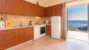 A kitchen with wooden cabinets, a stove, a sink, and a refrigerator. There is a balcony with a view of the sea. - Villa Marianthi with private pool  (2 Bedrooms, Sleeps 4) (Corfu, Peloponnisos Dytiki Ellada ke Ionio)