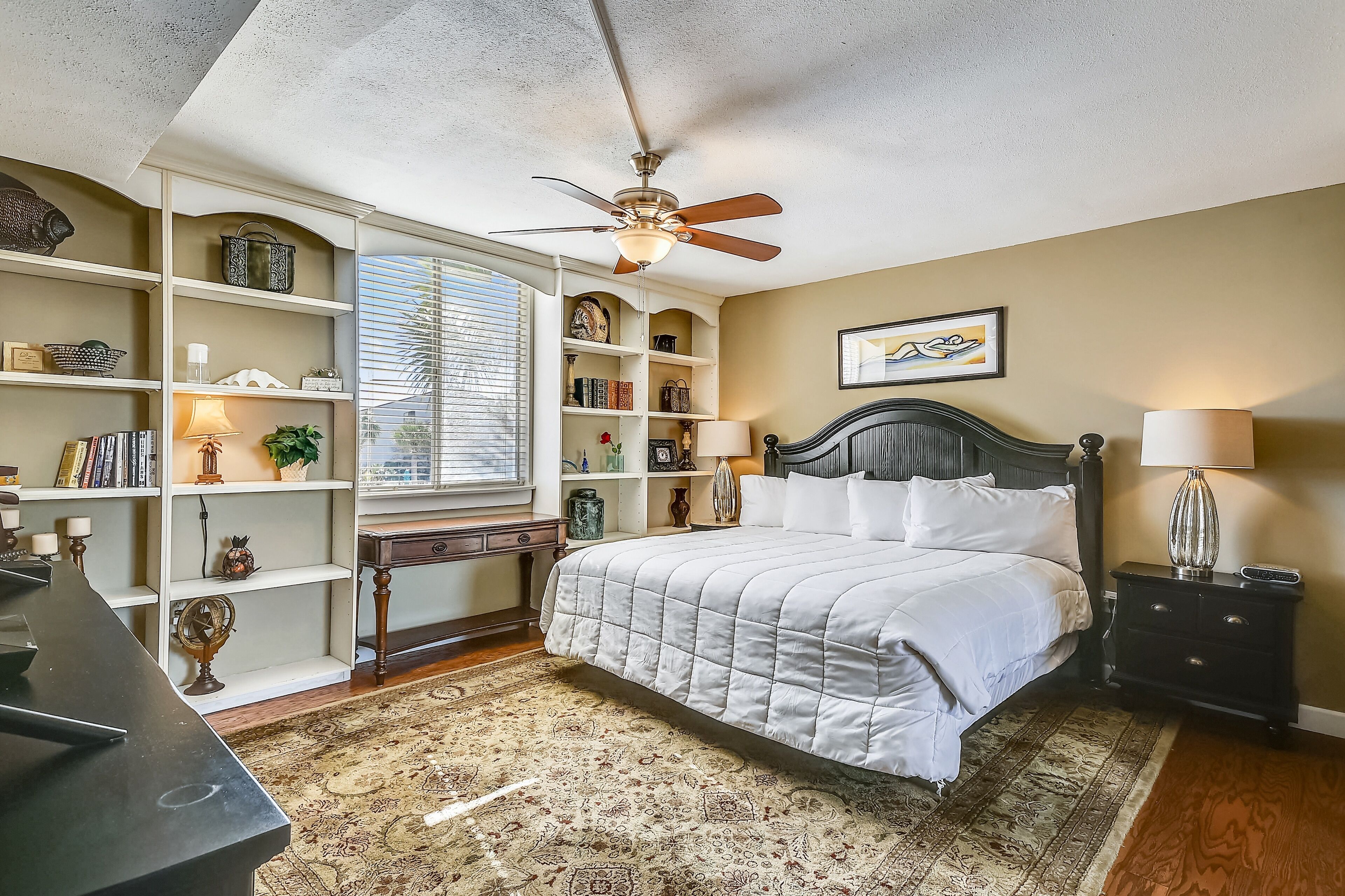 A bedroom with a bed, a ceiling fan, a bookshelf, and a desk.