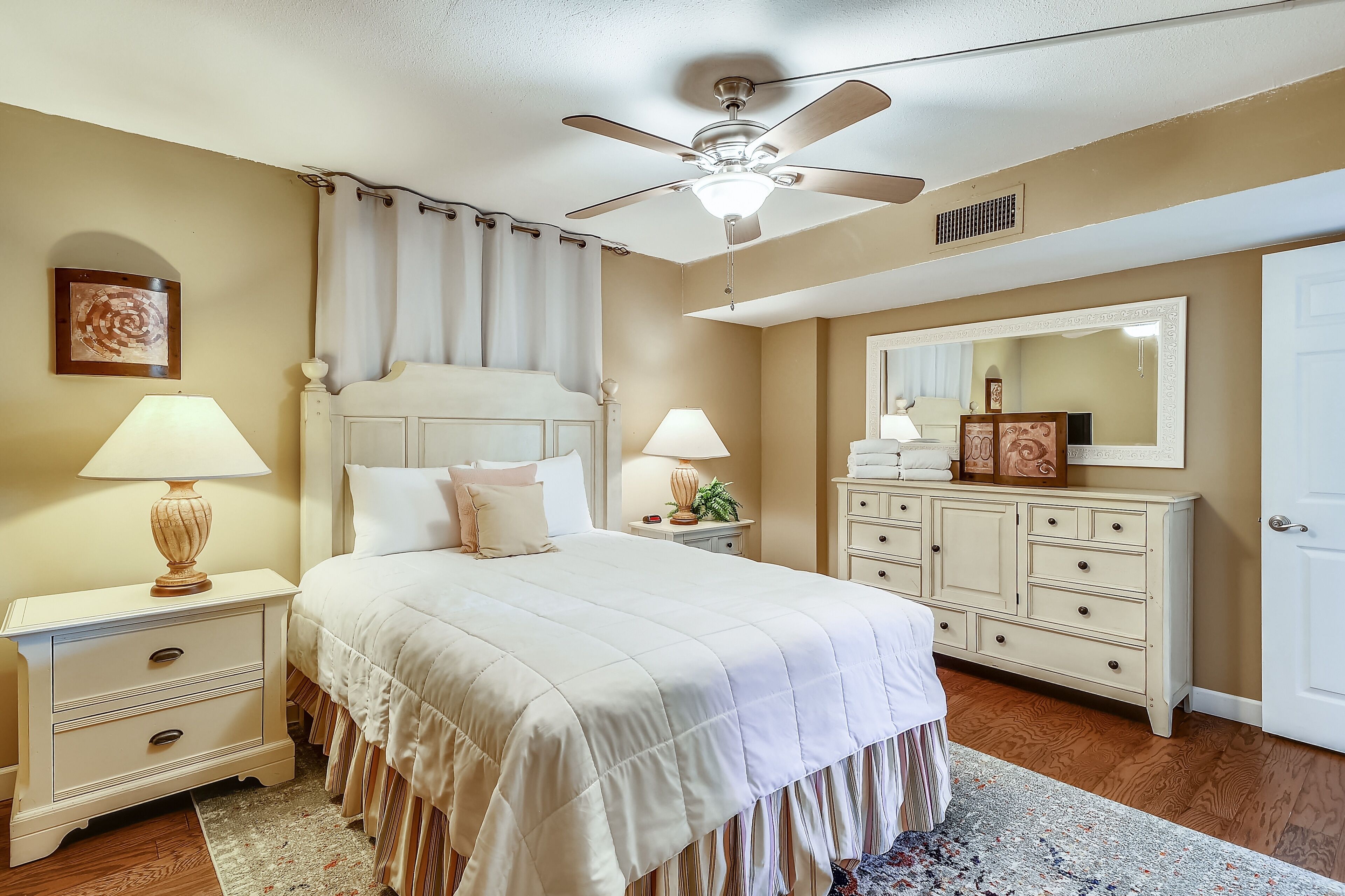 A bedroom with a bed, nightstands, a dresser, a ceiling fan, a mirror, and a door.