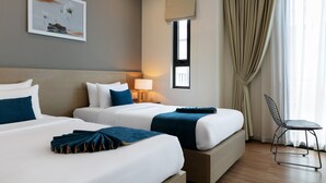 A hotel room with two beds, a chair, a lamp, and a window with curtains. - La Batisse Resort Halong (Bai Chay)