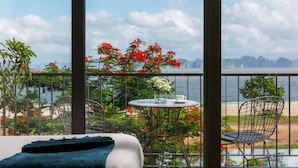 A balcony with a bed, a table with a cup and flowers, and chairs. - La Batisse Resort Halong (Bai Chay)