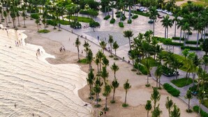 An aerial view of a beach with palm trees, people swimming, and a parking area. - La Batisse Resort Halong (Bai Chay)