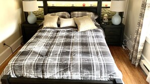 Een bed met een zwart-wit geruit sprei, twee nachtkastjes met lampen, en drie ingekaderde decoraties met veren aan de muur.