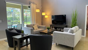 A modern living room with grey sofas, a flat-screen TV, and a dining area with a table and chairs. - Private Pool Oasis!  Ultimate Family Vacation! Solterra Resort Near Disney! (Davenport)