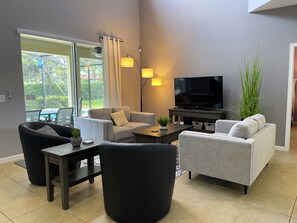 A modern living room with grey sofas, a flat-screen TV, and a dining area with a table and chairs.