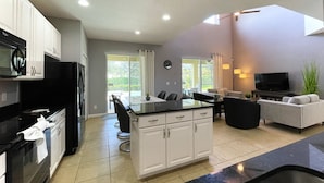 A modern kitchen with white cabinets, a black refrigerator, and a dining area with a glass table and chairs. - Private Pool Oasis!  Ultimate Family Vacation! Solterra Resort Near Disney! (Davenport)