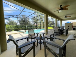 A covered outdoor area with a pool, seating, and a ceiling fan.