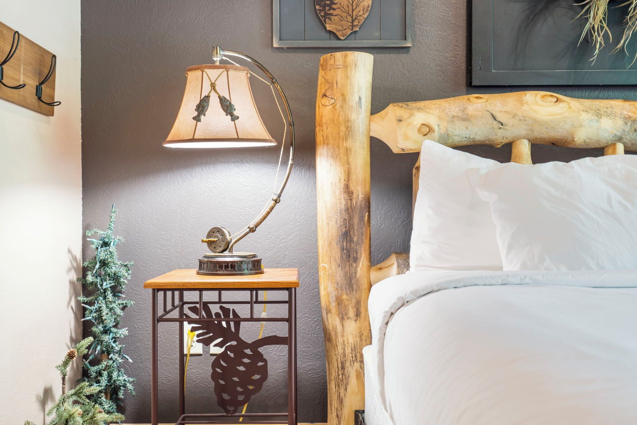 A neatly made bed with white linens, a wooden headboard, a small wooden nightstand with a lamp, and a decorative pineapple cutout.