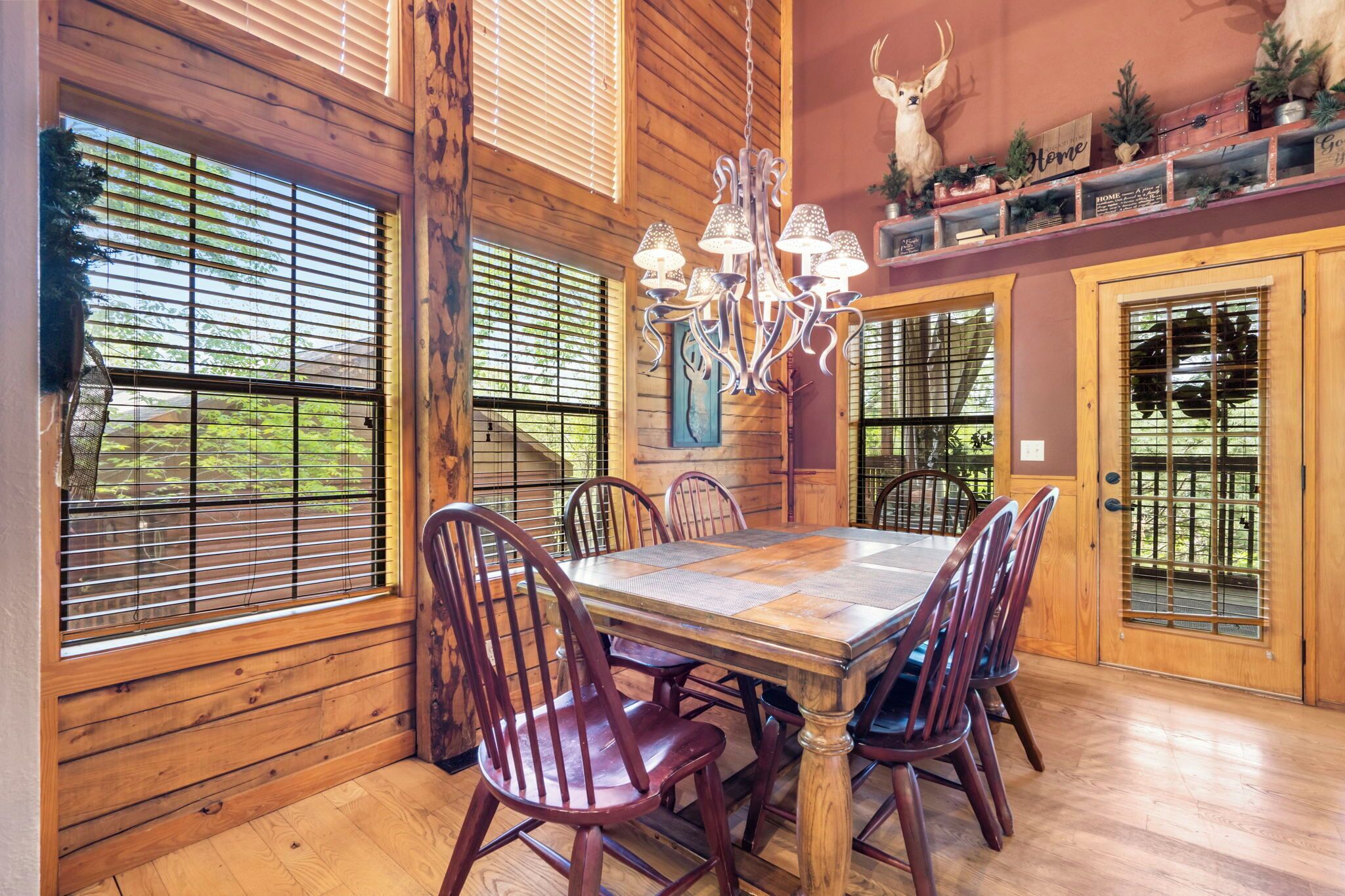 Un coin repas avec une table et des chaises en bois, un lustre et une décoration représentant une tête de cerf au mur.