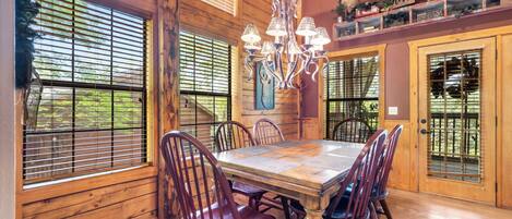 Un coin repas avec une table et des chaises en bois, un lustre et une décoration représentant une tête de cerf au mur.