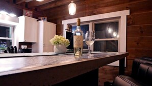 A wooden bar area with a bottle of wine and a glass on the counter, a vase with flowers, and a window in the background. - Rocky Top Retreat-Decorated for Christmas Near NPS (Victor)