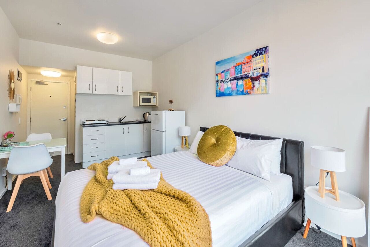 Una habitación de hotel con cama, escritorio, kitchenette y un cuadro en la pared.