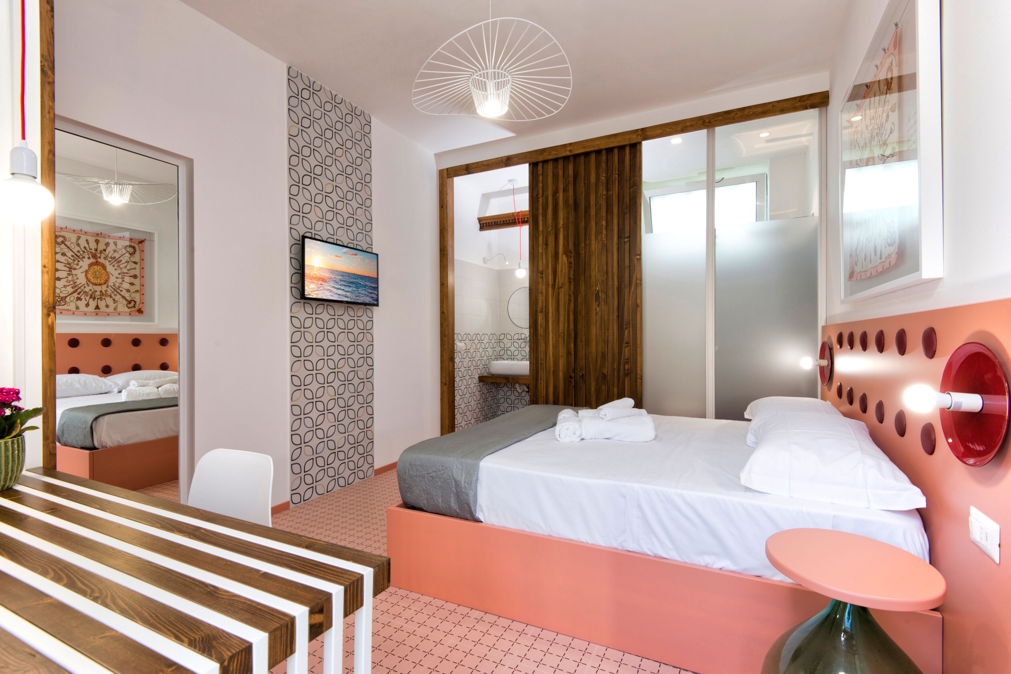A modern hotel room with a bed, bedside table, and a large mirror.