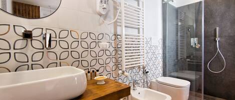 A modern bathroom with a large white sink, a wooden vanity, a bidet, a glass-enclosed shower, and a towel rack.