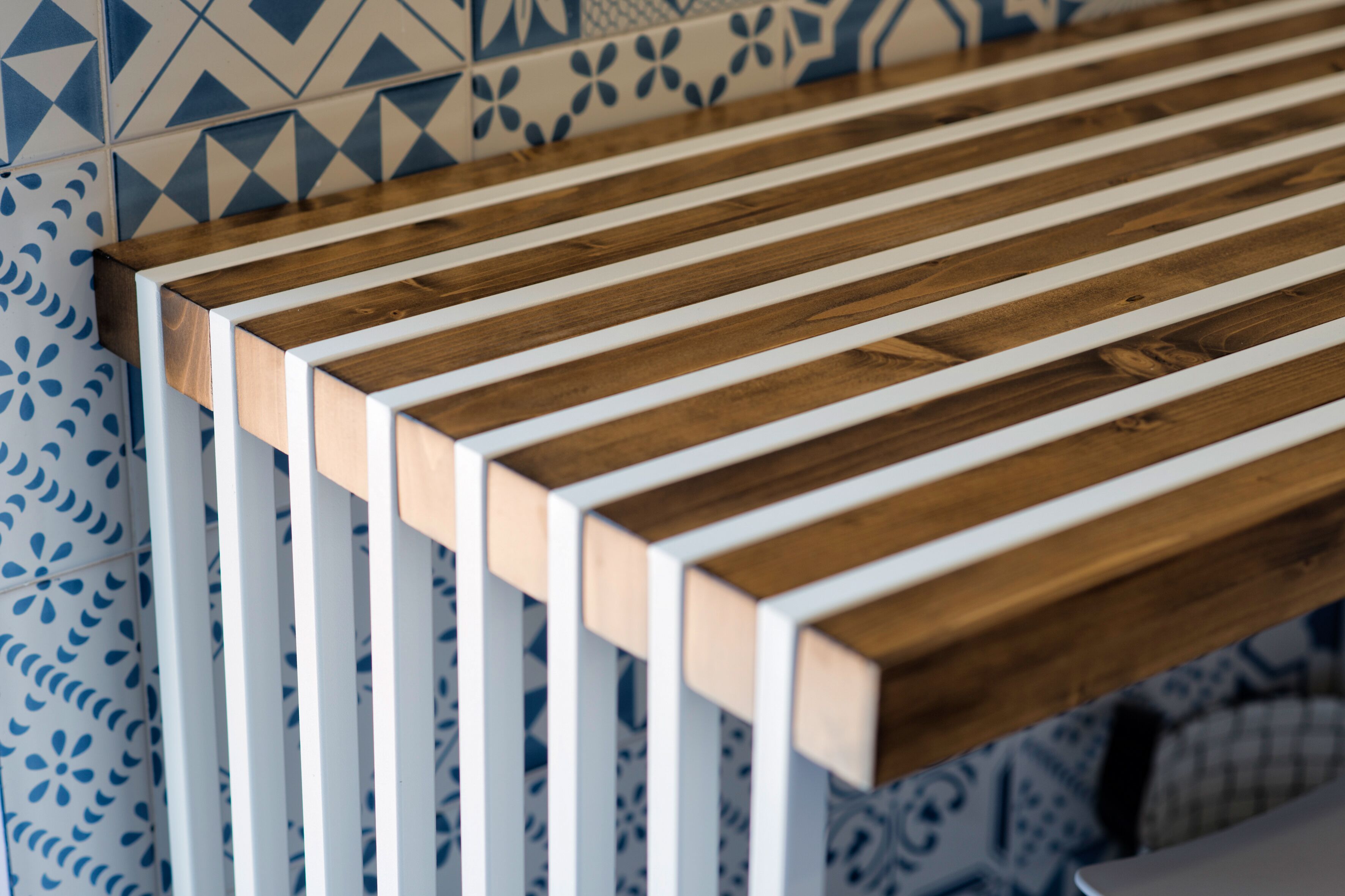 Un banc en bois doté de supports verticaux blancs, adossé à un mur carrelé orné de motifs géométriques.