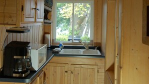Eine Holzhütte mit einer Küche, die ein Fenster, Holzschränke, eine Kaffeemaschine und eine Mikrowelle beinhaltet.