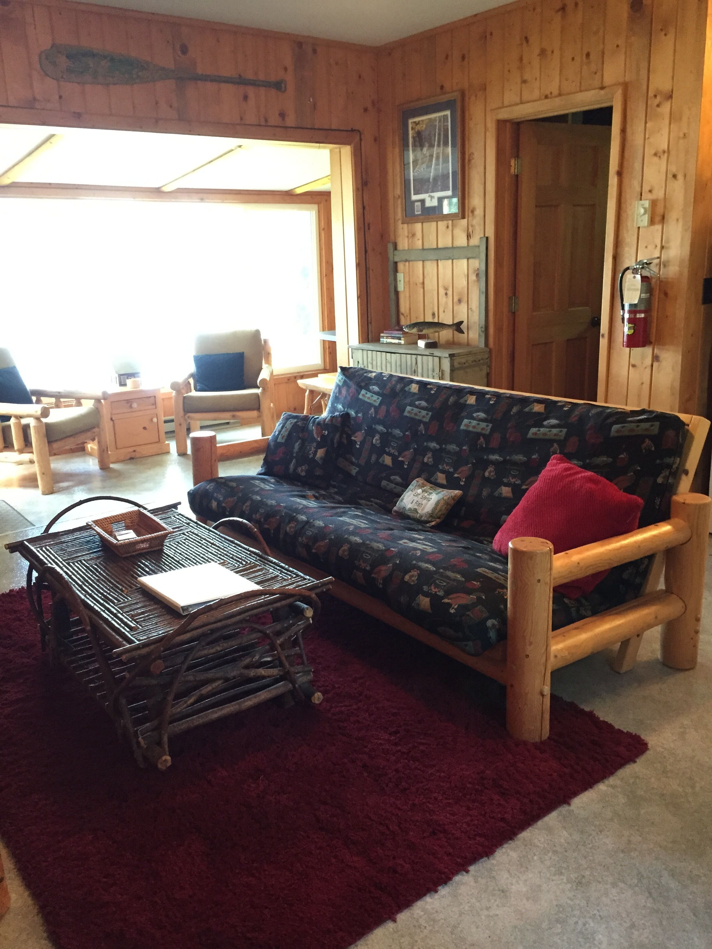 A cozy cabin interior with a wooden sofa, a small table, and a red rug.