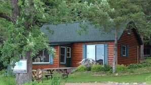 Eine rustikale Holzhütte mit Picknicktisch, umgeben von viel Grün und einem klaren Pfad.