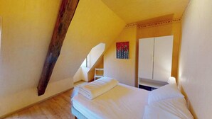 Une chambre avec un plafond en pente, un lit, une chaise et une armoire.