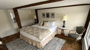 Un dormitorio con una cama grande, una silla, una mesita y una ventana.