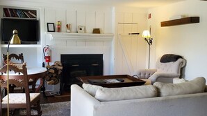 Una sala acogedora con chimenea, un sofá, una mesa de comedor con sillas y una estantería.