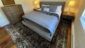 A bedroom with a bed, a dresser, and two bedside lamps. - Deluxe King, Living Room w/sofa bed & fireplace (Dover)