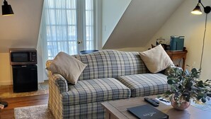 A cozy living room with a plaid sofa, a coffee table, and a potted plant. - Deluxe King, Living Room w/sofa bed & fireplace (Dover)