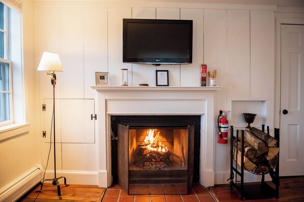 A fireplace with a TV above it, a lamp to the left, and a fire burning.
