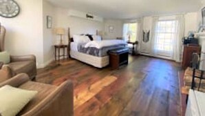 Een ruime kamer met een groot bed, een houten vloer, een stoel en een bureau.