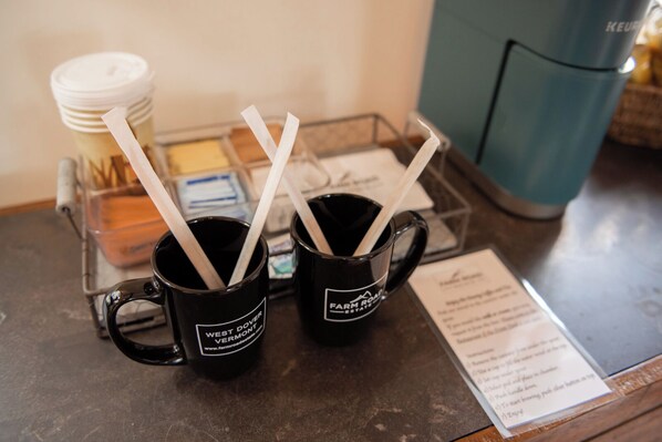 Two black mugs with white text and straws on a metal tray.