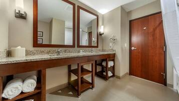 Uma casa de banho de hotel com uma pia dupla, dois espelhos, um porta-toalhas com toalhas, área de duche e uma porta de madeira.