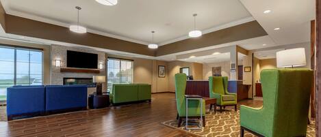 A spacious lobby with a flat-screen TV, green seating, and a patterned carpet.