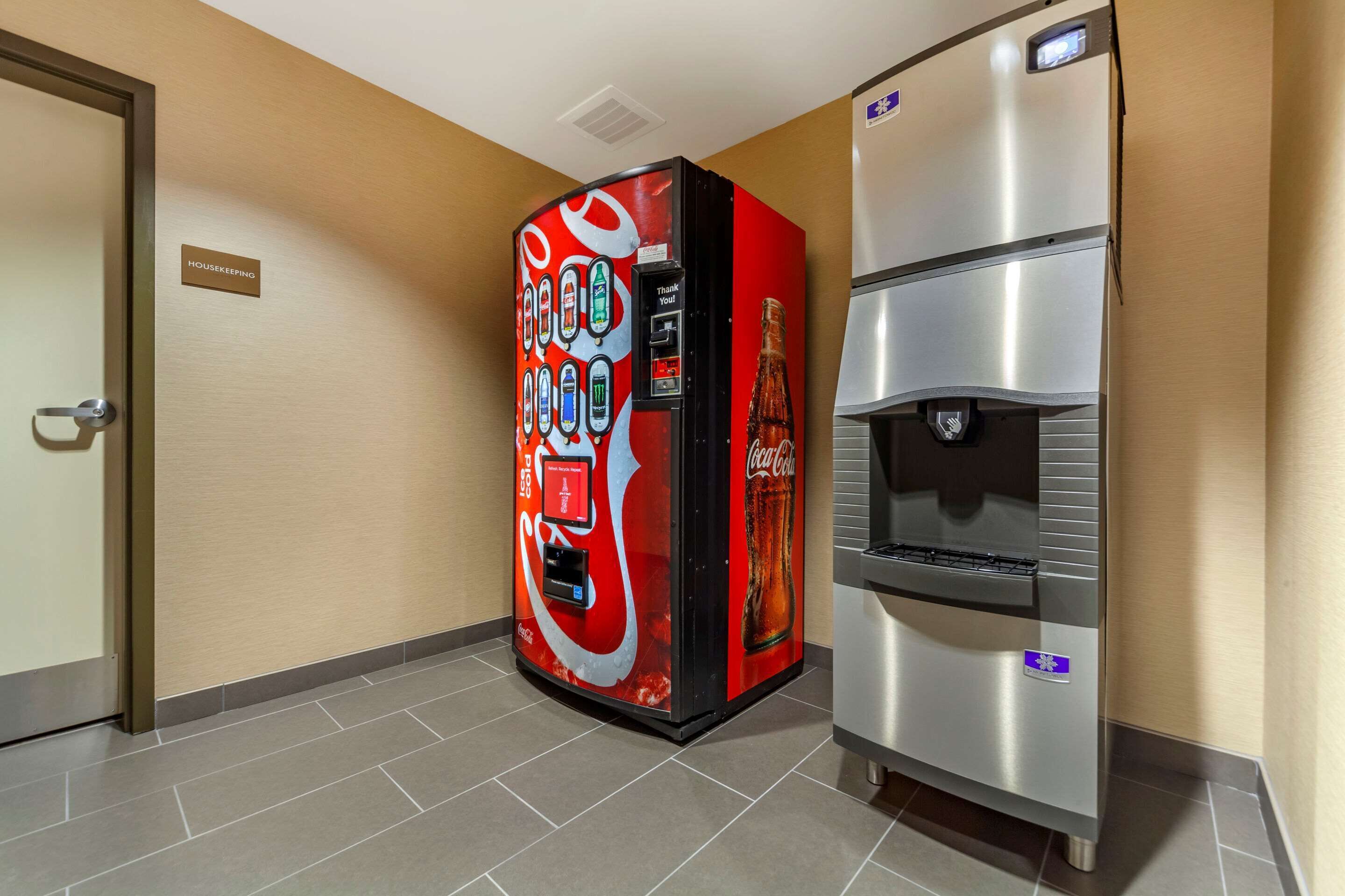 A vending machine with a Coca-Cola logo, a water dispenser, and a housekeeping sign on the wall.