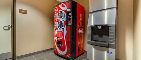 En salgsautomat med Coca-Cola logo, en vanddispenser og et skiltegn for rengøring på væggen.